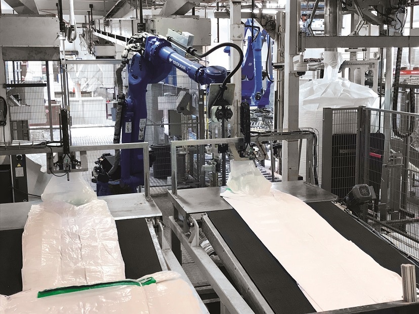 Roboter in einer Industriehalle befüllt einen Bigbag, der wie ein Schlauch auf einer Art Tisch liegt.