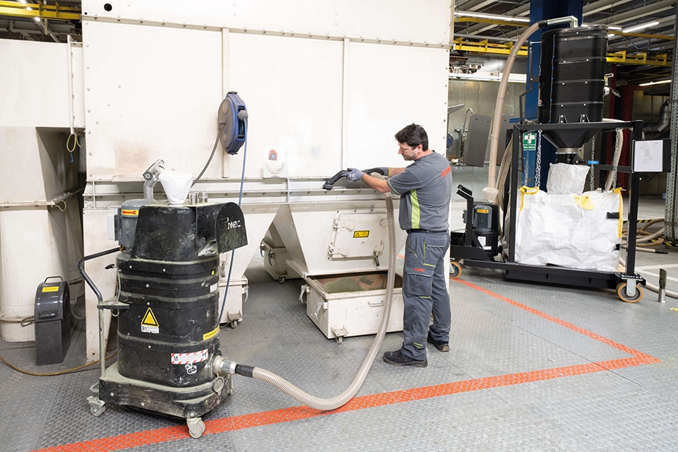 Ein Mitarbeiter in einer Industriehalle saugt mit einem Industriesauger eine Auffangwanne einer Maschine ab.