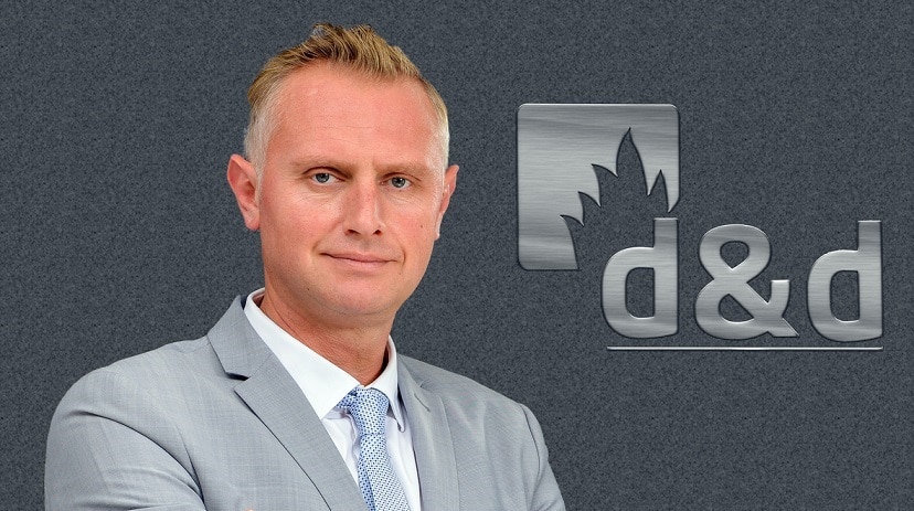 Ilija Divkovic vor einer grauen Wand mit einem Logo d&d davor.