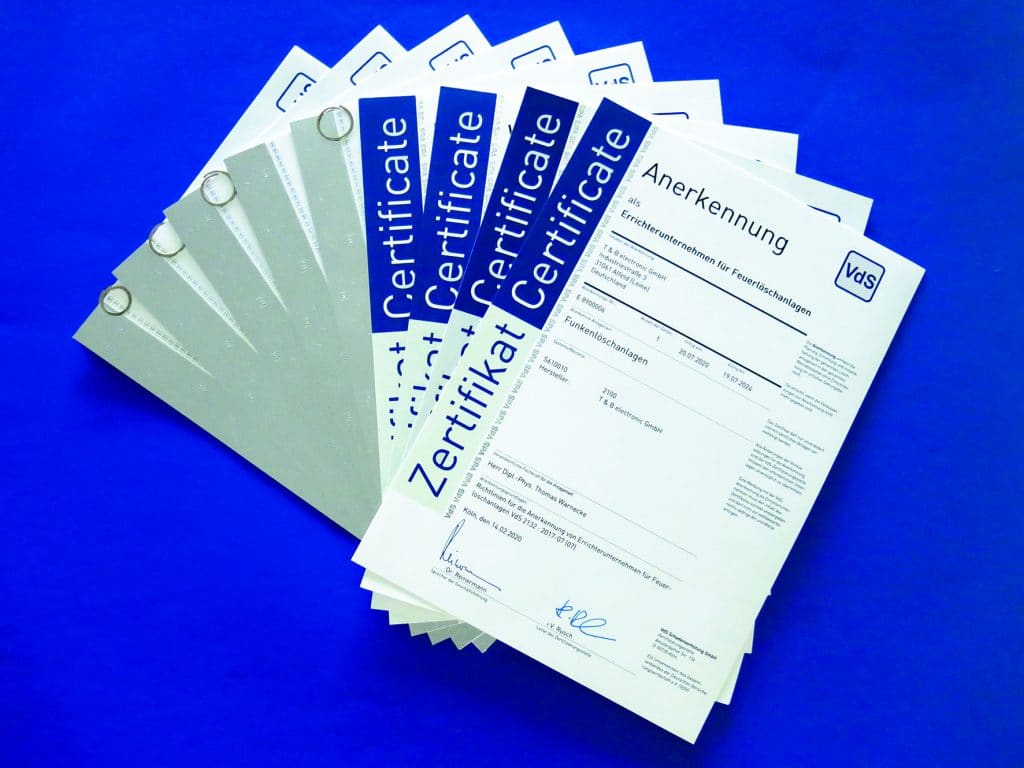 Diverse VdS Zertifikate liegen in Fächerform auf einem blauen Hintergrund