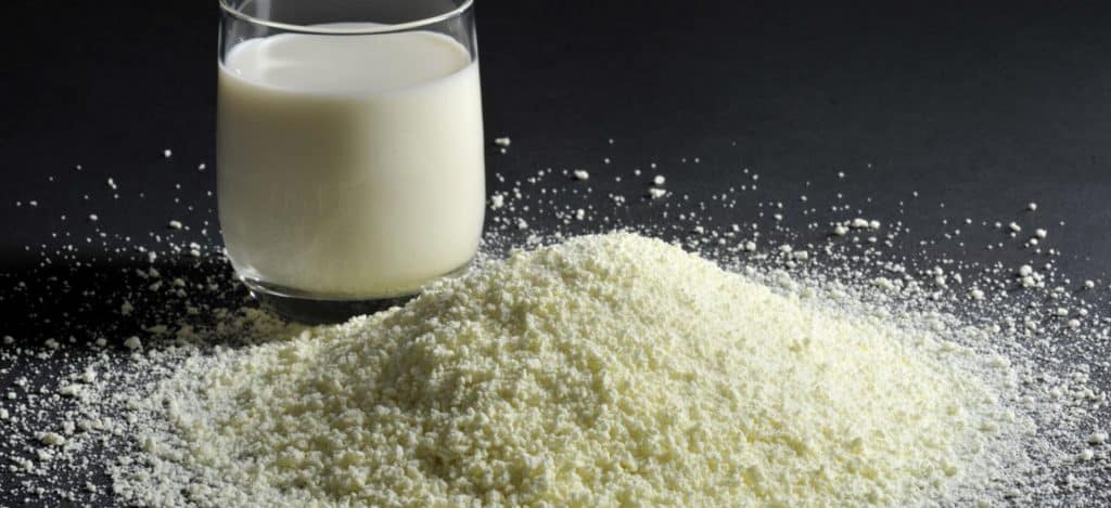 Ein Glas Milch auf schwarzem Untergrund mit Milchpulver davor, auf schuettgutmagazin.de