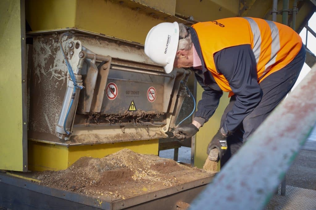 Mann steht mit Rücken zu uns und öffnet Schacht an Maschine