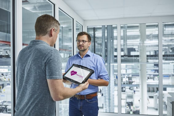 Mitarbeiter halten in einem Raum über einer Werkshalle ein Tablet in der Hand auf der die Software der E+H für Heartbeat Technology zu sehen ist, auf schuettgutmagazin.de