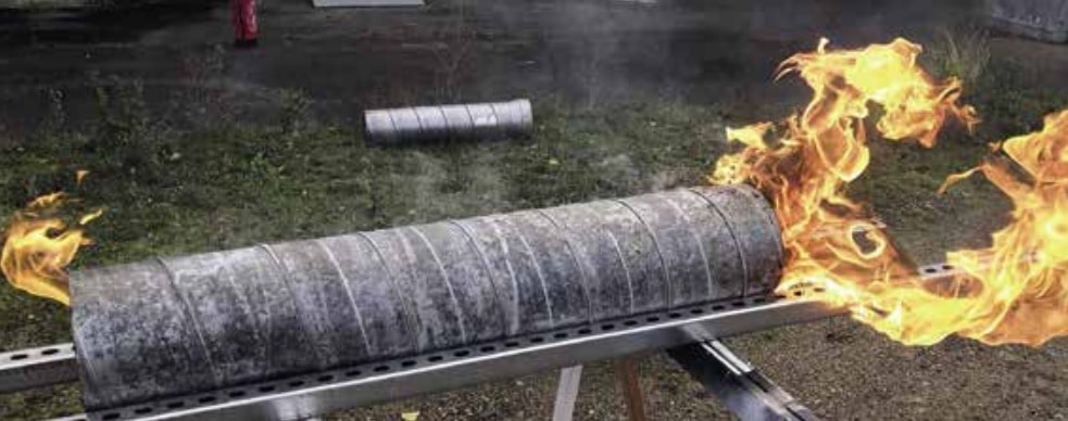 Aufgebockt auf Metallstreben ist zur Verdeutlichung der Dynamik eines Rohrbrandes unter Ausnutzung der Windrichtung ein demontiertes Rohrstück zu sehen. Links flammt es in kleiner Flamme aus dem Rohr, rechts mit sich spaltenden großen Flammen.