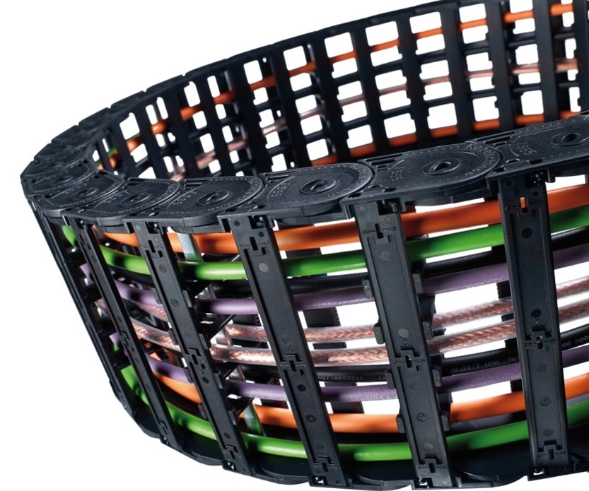 Kabel in einer flexiblen Schutzhülle aus Plastik. Einzelteile sind aus Stäben und seitlicher Führung gefertigt. Tsubaki Kabelschlepp auf schuettgutmagazin.de