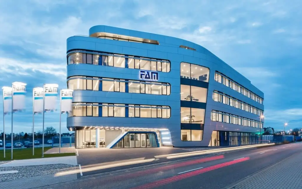 Gebäude in Schiffsform der FAM Gruppe im Zwielicht, mit Straße davor und Lichtreflexen, die Geschwindigkeit implizieren.