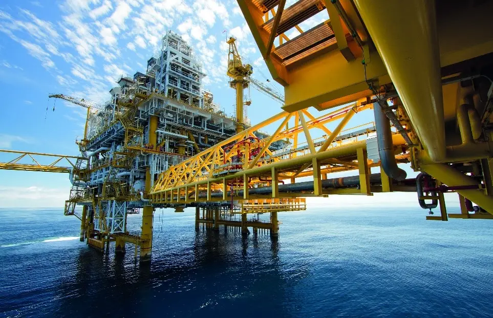 Mehrstöckige Bohrinsel mit gelben Stahlträgern im Meer. Im Hintergrund ein Teil, in den Vordergrund ragend ein Übergang zum vorderen Teil, der auch mehrstöckig zu sein scheint.