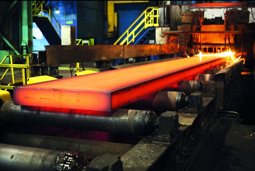 Stahlblock auf einem Hengstler Drehgeber in einem Industriebau. Im Hintergrund eine Maschine, die die Oberfläche des Stahlblocks behandelt.