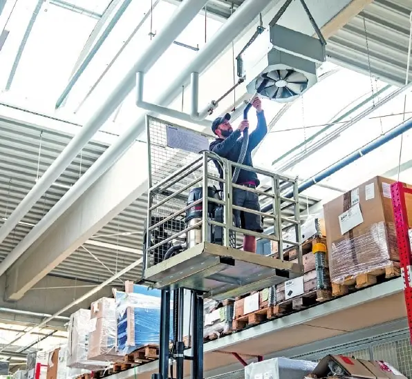 In einer Industriehalle saugt ein Mann auf einer Hebebühne ein Belüftungsventil aus.