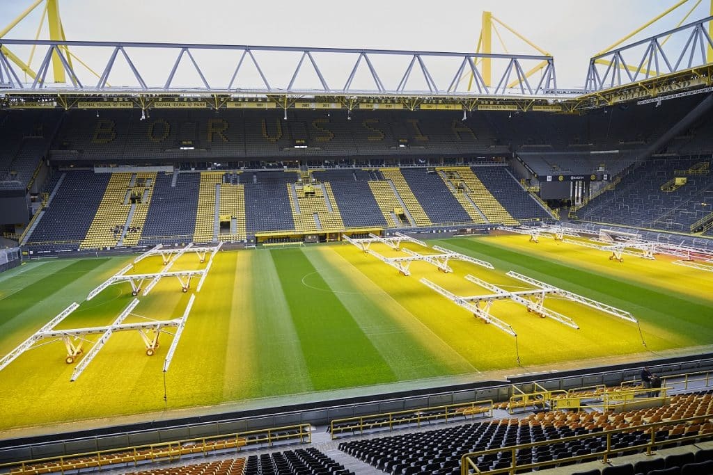 Blick auf das BVB Stadion aus der Loge - der Rasen ist durch Licht in Gelb und Grün gestreift. darauf stehen Bewässerungs-Maschinen