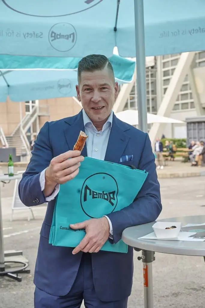 Stefan Penno mit einer Bratwurst in der rechten Hand und einer grünen Rembe Tasche auf dem Außengelände der Solids 2023