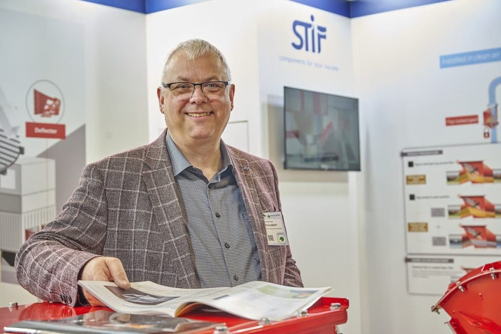 Thomas Schubert der STIF France auf dem Messestand, vor ihm ein Heft der Schüttgut & Prozess, in dem ein Artikel der STIF veröffentlicht ist.
