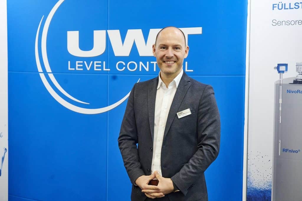 Kevin Walter, UWT auf der Solids 2023 vor einem UWT Logo neben einem Messebild.