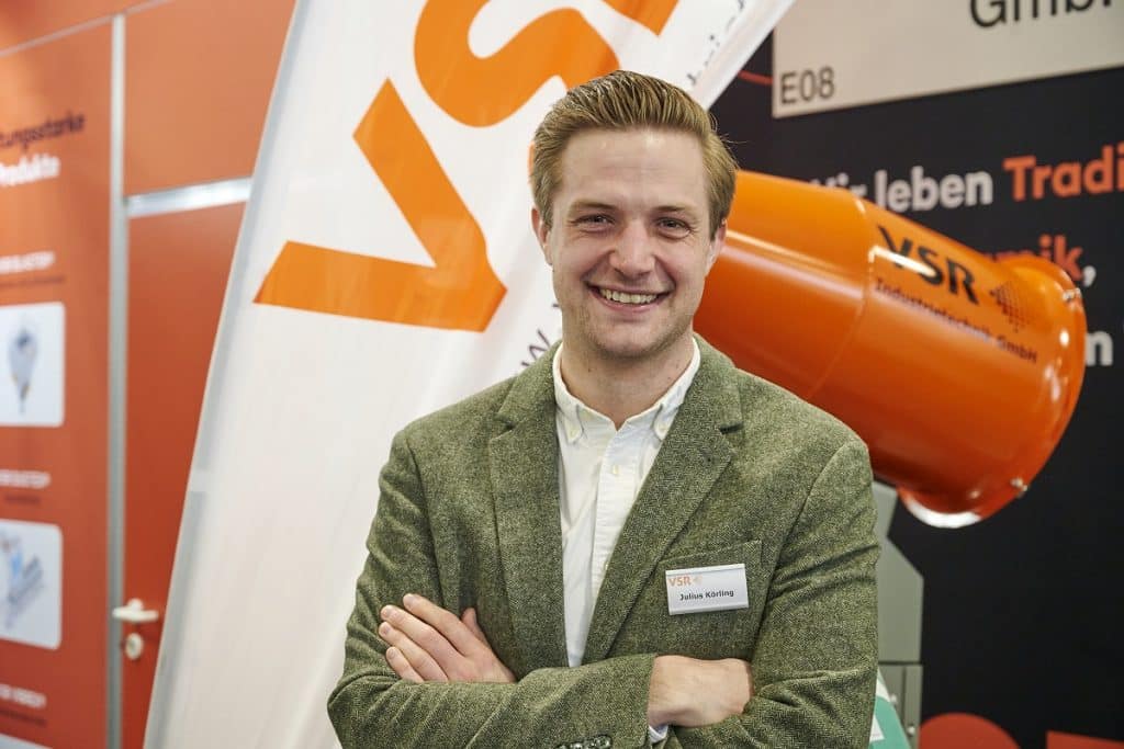 Julius Körling vor einem orangenen VSR Produkt auf dem Messestand der Solids 2023