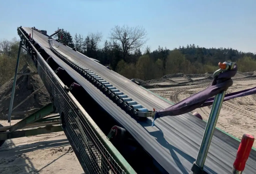 Im Außengelände sieht man ein Förderband mit Prüfkette darauf. Diese dient zum Abgleich der Bandwaage.