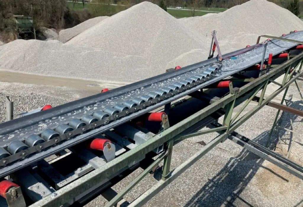 Förderband mit einer Prüfkette darauf auf einem Außengelände mit Schotter. So wird die Bandwaage geprüft.
