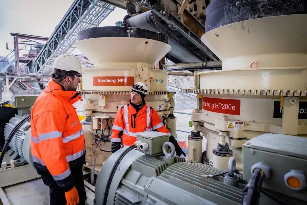 Mitarbeitder der Nordberg stehen zwischen zwei Kegelbrechern im Außengelände