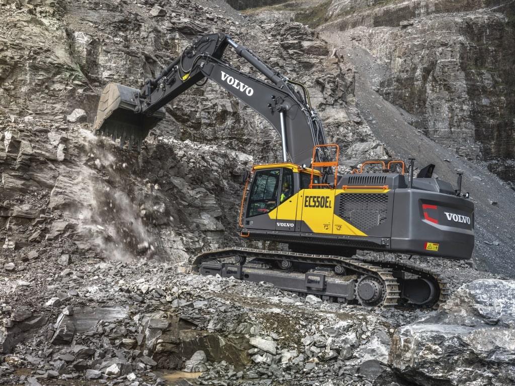 Volvo Kettenbagger in einem Steinbruch mit dunklem Gestein am Abschaufeln aus der Höhe.