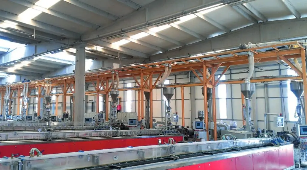 Industriehalle mit einer Mehrstellenbeschickungsanlage mittels Spiralförderer. Im Hintergrund ein gelbes Gestänge mit Dosiereinheiten davor Spiralförderer rot verkleidet.