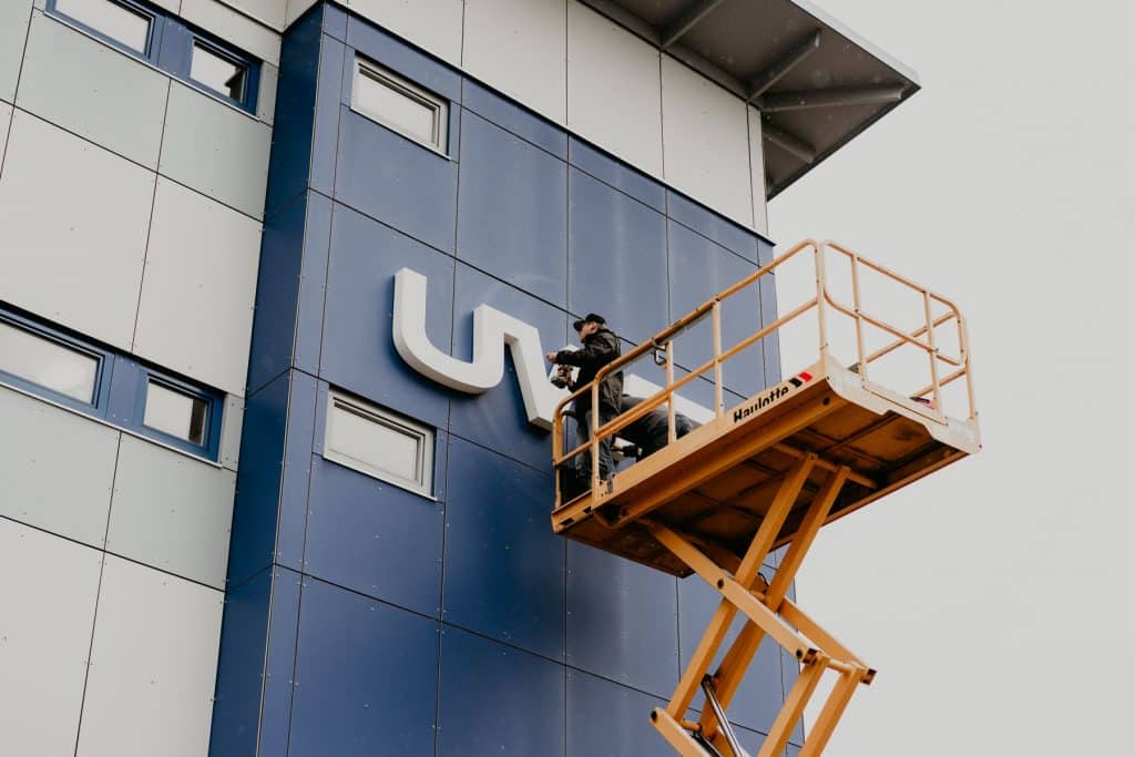 Auf einem Hubwagen bringt ein Arbeiter das neue Logo der UWT an einer blau verkleideten Wand des Firmengebäudes an.