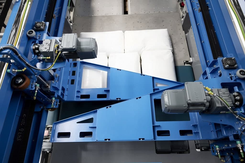 Packmaschine von oben. Zwei verschiebbare Elemente über 5 Packeten, die verpackt werden sollen.