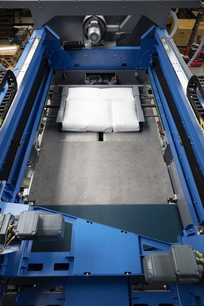 Packmaschine paletpac. In der Mittel liegt ein Produkt das verpackt wurde rechts und links vom Paket Schieber darunter viel Platz für ein größeres Produkt. Darüber Kabelschlepper ,die die Mechanik der Packmaschine mitmachen.