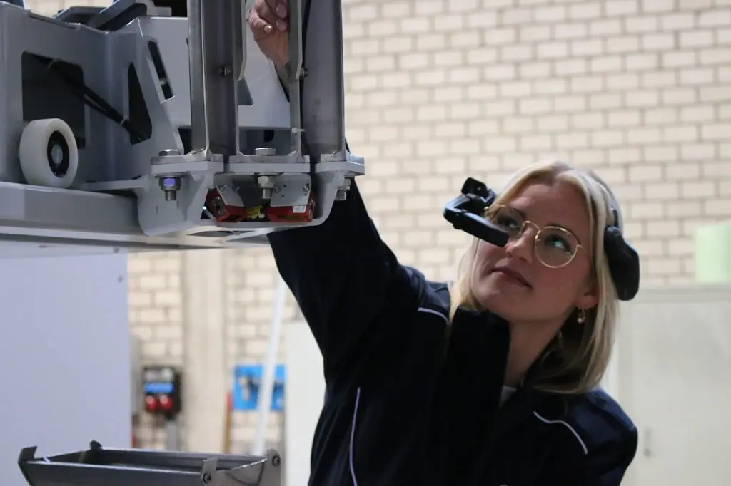Eine Technikerin trägt eine Smart Glasses Kamera der BEUMER Group und korrigierte ein Element einer Anlage.
