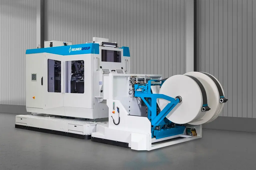 Maschine der BEUMER Group, die aussieht, wie ein Schlitten auf dem hinten ein Kasten mit Fenster ist und vorn zwei unterschiedlich große Rollen, die den Boden nicht berühren. Die Technik, die den Inhalt der Rollen mit den Vorgängen im Kasten verknüpft..