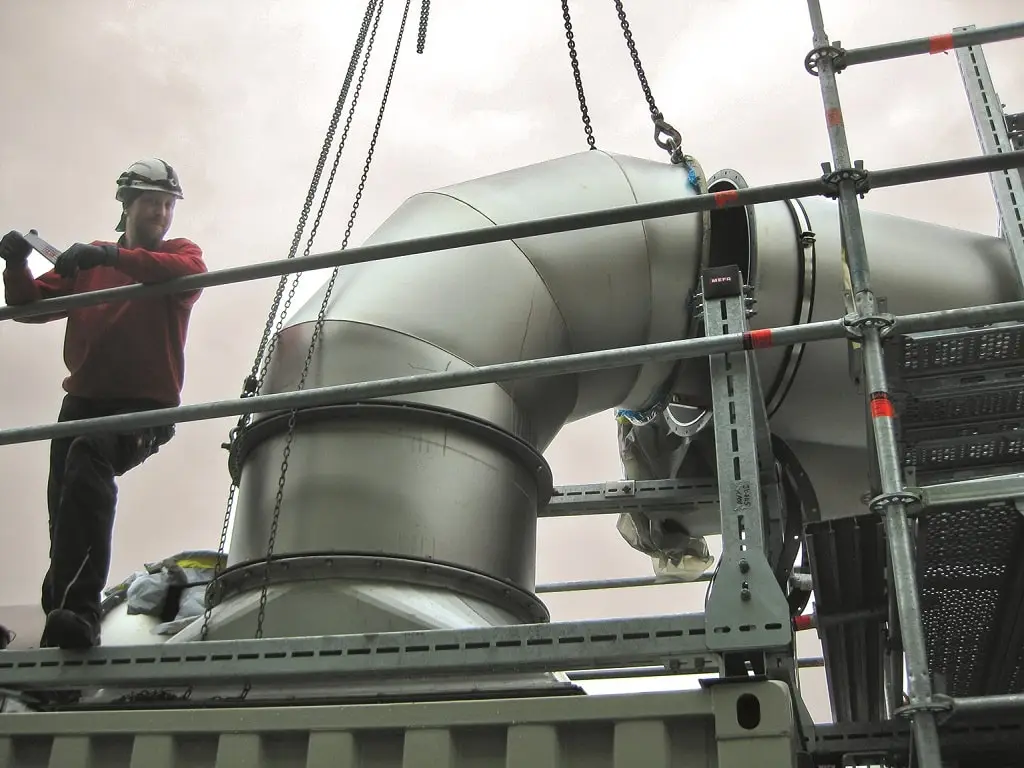 Auf dem Dach eines Industriegebäudes steht ein Mitarbeiter der Jacob Rohre und montiert ein Belüftungsrohr an einem 90° Rohrbogen.