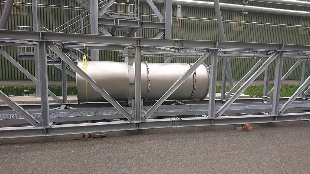 Ein Rohrstück, DIN 1250, auf einem Schienensystem liegt auf einem Außengelände vor einer Industriehalle.