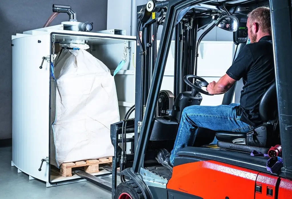 Gabelstaplerfahrer, rechts, fährt an eine Aufbewahrung für einen Big-Bag Sauggut-Beutel. Dieser steht auf einer Europalette.