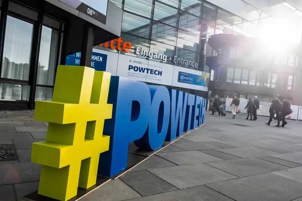 Vor der Messehalle Eingang Mitte der Messe Nürnberg steht ein gelbes Hashtag und dahinter in großen blauen Buchstaben POWTECH. Im Hintergrund sieht man Menschen auf die Halle zulaufen.