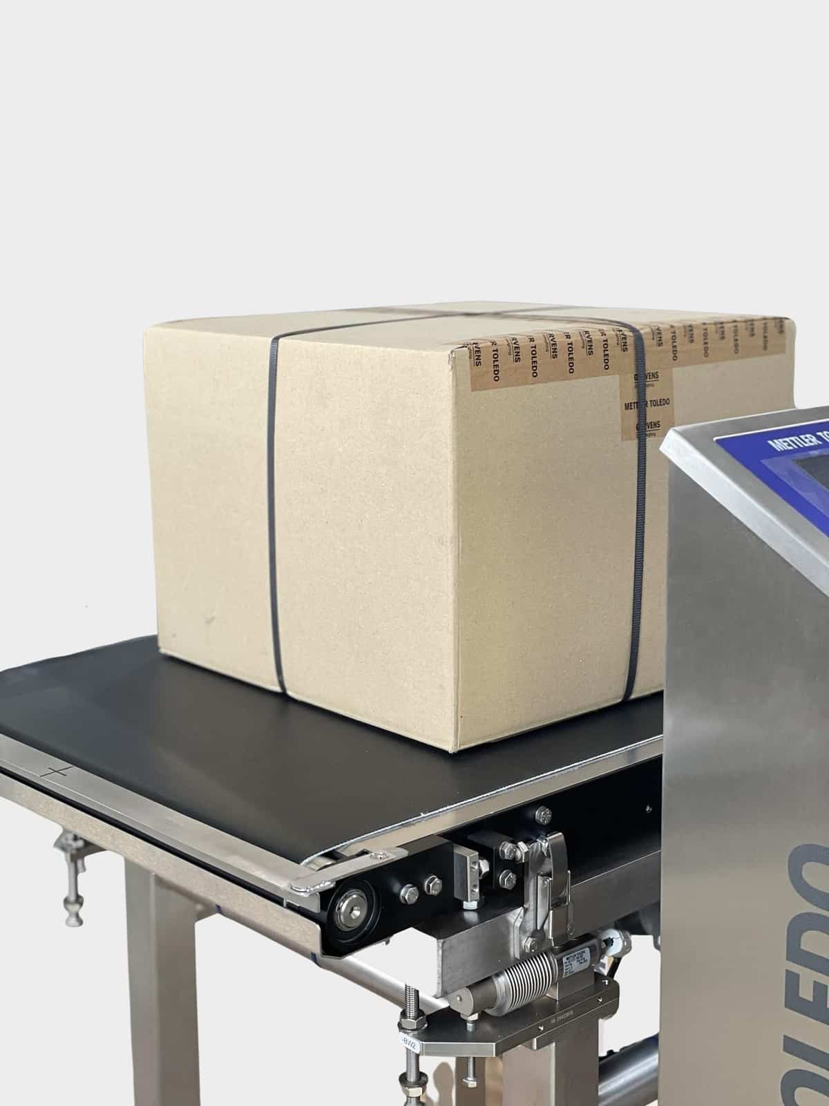 Paket steht auf dem Laufband einer Kontrollwaage. Rechts sieht man noch einen Teil des Steuerungselementes.
