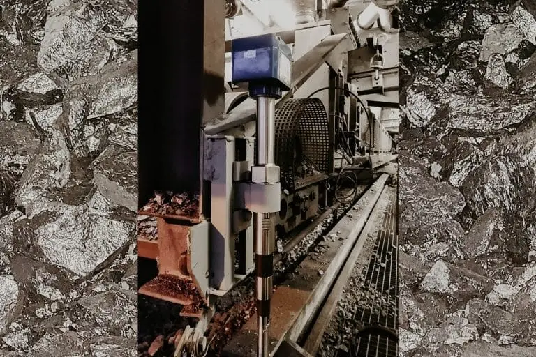 Schmales Bild, das durch glänzende Kohlestücken verbreitert wurde. Man sieht dort ein Produktionsabschnitt von Siliziummetall in dem ein Grenzstandsmesser eingebaut ist.