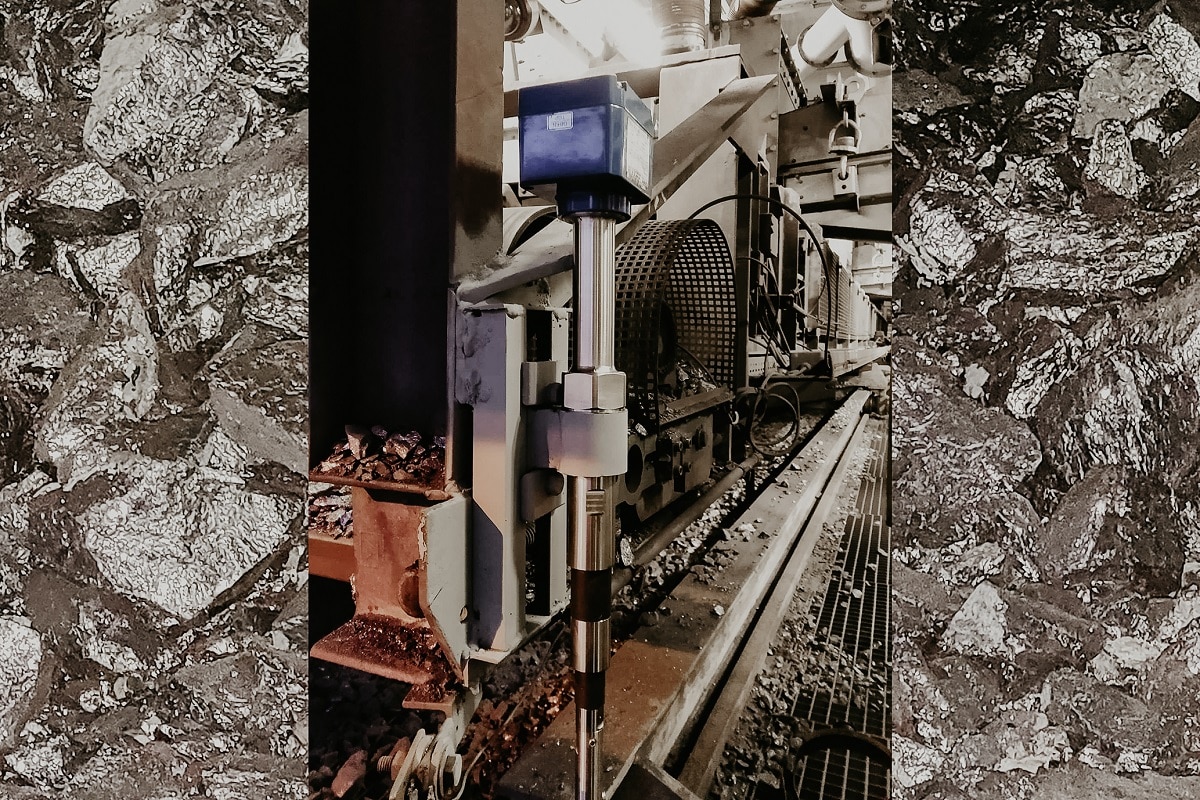 Schmales Bild, das durch glänzende Kohlestücken verbreitert wurde. Man sieht dort ein Produktionsabschnitt von Siliziummetall in dem ein Grenzstandsmesser eingebaut ist.