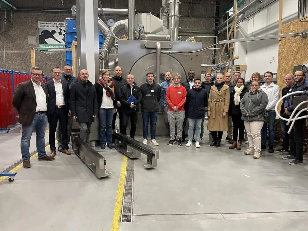 Gruppe von Mitarbeitern und Mitarbeiterinnen steht in einer Industriehalle vor einer Industriemaschine.