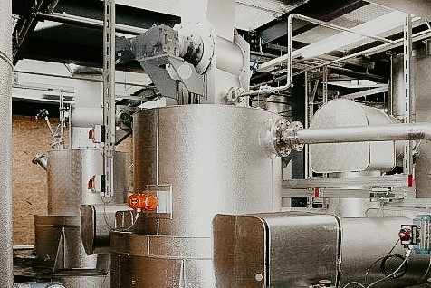 Doppelfeuervergasungsreaktor in einer Industriehalle. Silberne unterschiedlich große Behältnisse, die mit einem Rohr verbunden sind.
