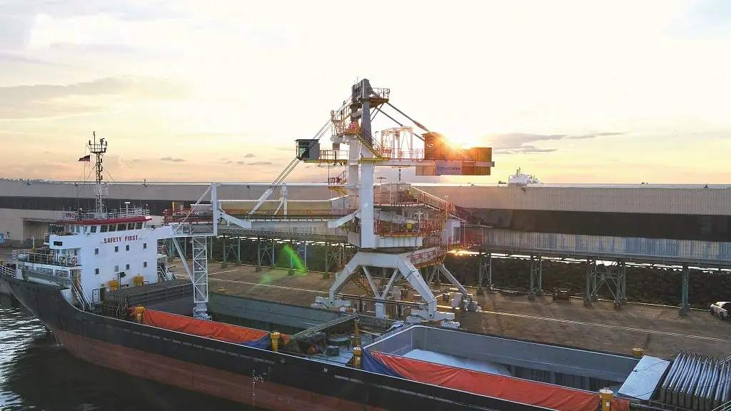 Schiff an einem Hafenterminal, das über mehrere Stockwerke hoch ist. Davor angelegt ein Schiff mit großen Ladeflächen.