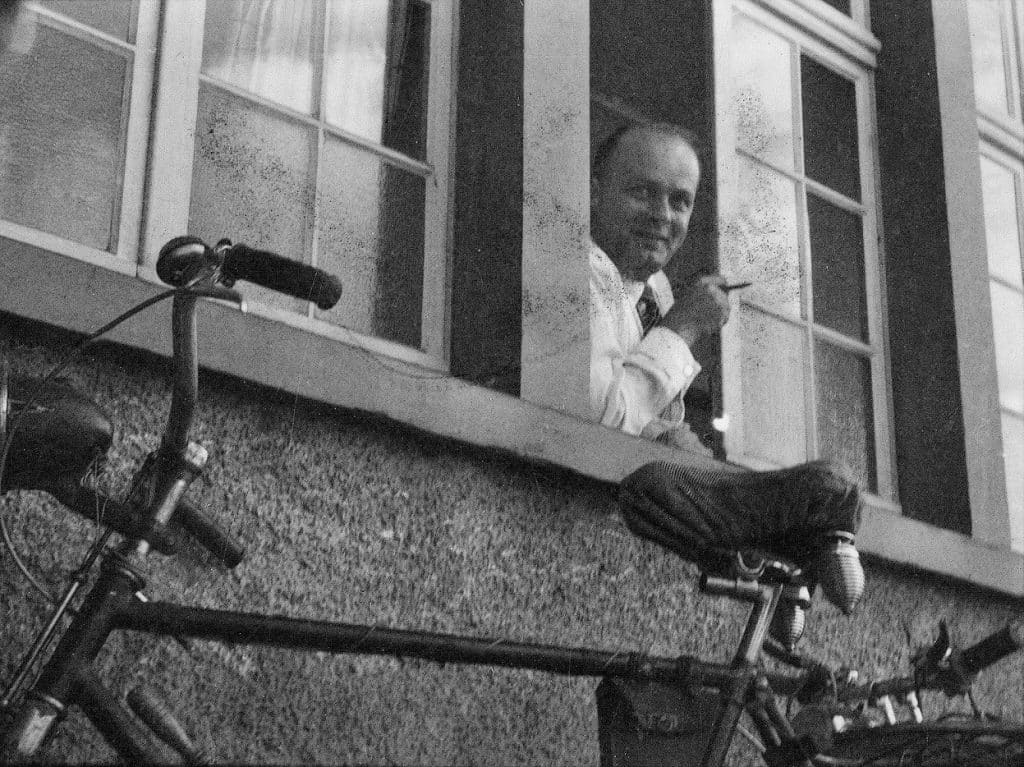 Georg H. Endress als junger Mann auf einem schwarz-weiß Foto. Er schaut im Hemd rauchend aus einem der drei sichtbaren Fenster. Unter ihm steht ein Fahrrad. Die Bild ist aus der Reifenhöhe nach oben fotografiert.