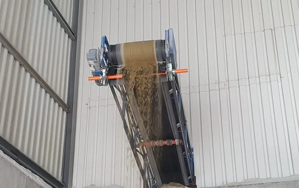 Ein Förderband in einer Industriehalle wirft Sand ab. Das Förderband wird mit einem Förderbandabstreifer gereinigt.
