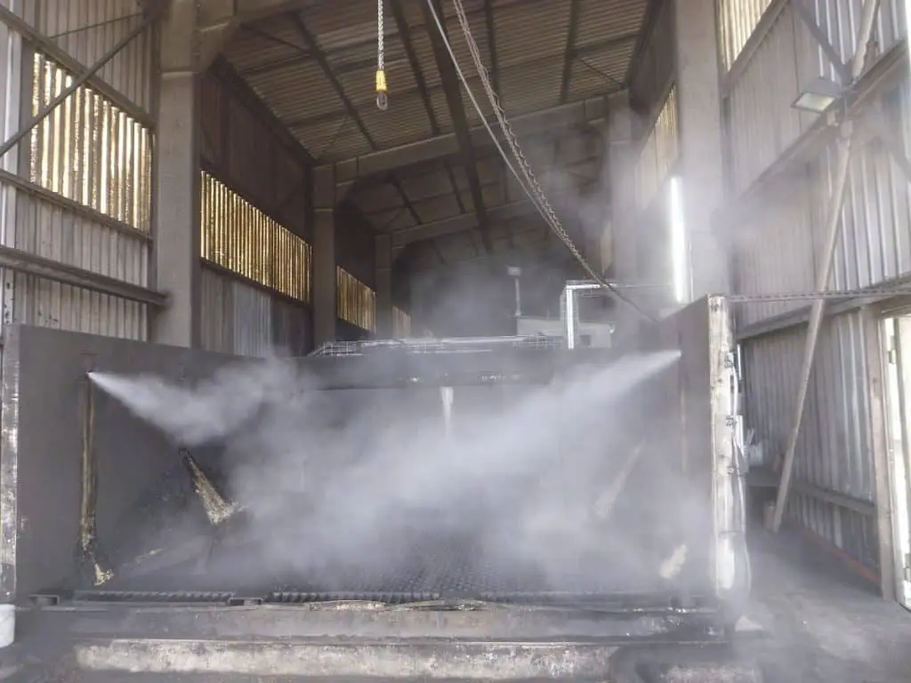Durch Düsen wird Wassernebel auf die Entladefläche eines Lastwagens gesprüht, darüber eine Industriehalle.