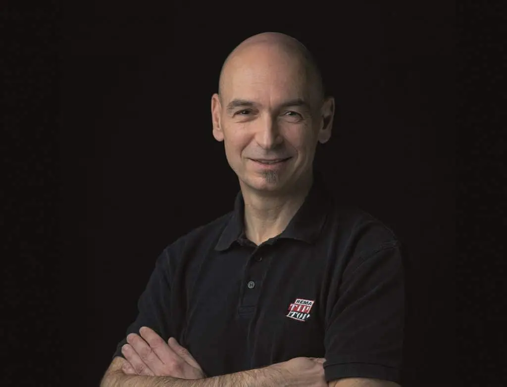 Klaus Dieter Brandl vor schwarzem Hintergrund mit schwarzem Polo, das eine REMA TIP TOP LOGO aufgenäht hat.