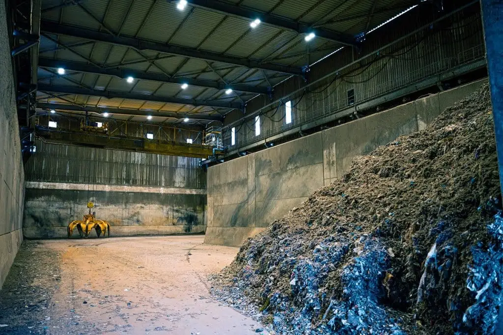 In einer Industriehalle liegt rechts vorn brennbares Gut. Hinten links ist ein Greifarm, der das Schüttgut bewegen kann.
