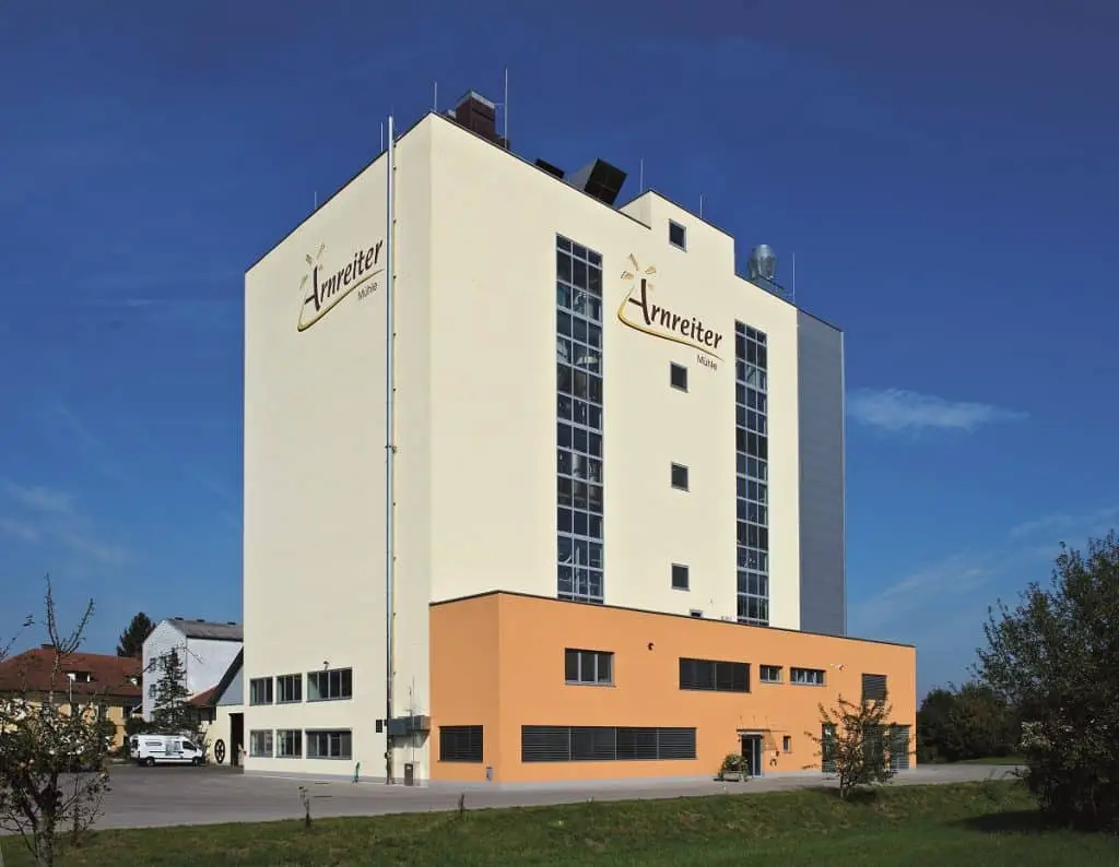 Mühlengebäude der Anreiter. Ein rechteckiges, sehr hohes Gebäude. Davor ist ein ocker gestrichener Anbau. Im Hintergrund links sieht man ältere Gebäude und einen Kastenwagen.