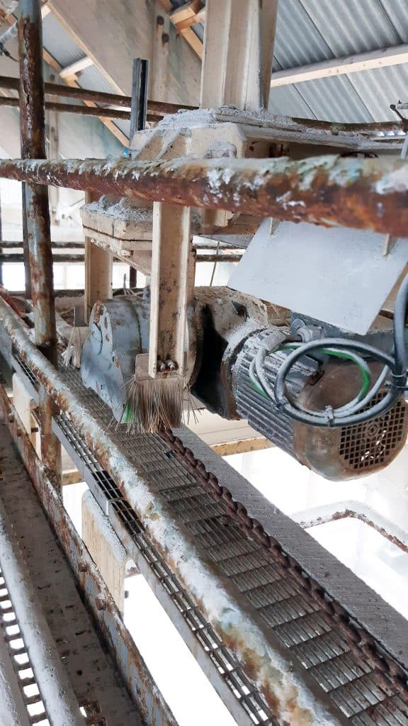 In einer Industriehalle ist ein Bandabsetzer mit viel Salz an den Rohren und Rost zu sehen. Im Vordergrund ein Antriebsgerät.