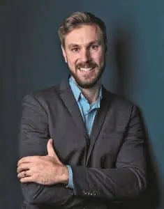 René Schwertfeger von der T&B electronic. Er steht und hat ein blaues Hemd und einen grauen Anzug an, der dezente weiße Karo-Linien hat.