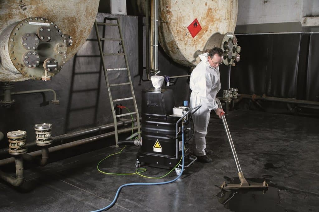Ein Mitarbeiter mit einem weißen Anzug saugt eine Flüssigkeit vom Boden.