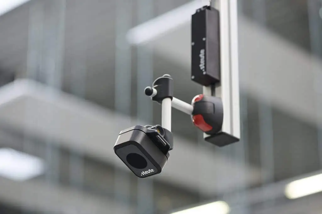 Lasersensor hängt an einem Metallstab von der Decke, mit einer Vorrichtung, die erst eine horizontale Stange hat, an der eine Vertikale hängt. An dieser wiederum ist der Sensor angebracht.