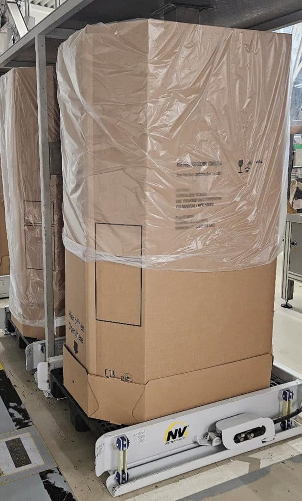 Großer Karton auf einem Vibrationstisch, in dessen inneres ein großer Plastiksack eingestülpt ist.