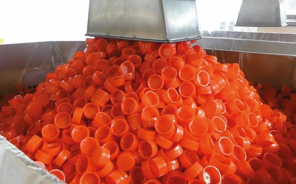 Rote Kunsstoff Plastikdelckel werden über einen Stutzen in einen Metallcontainer mit ausgelegter Folie gefüllt.